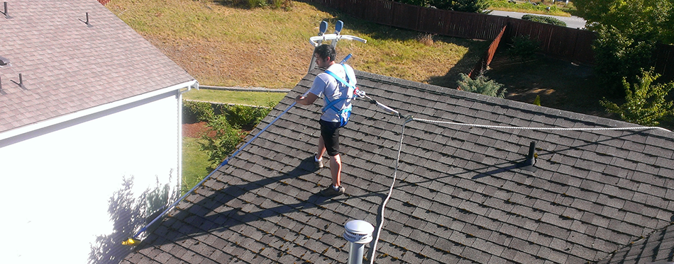 A man on the roof of a house with a hose.